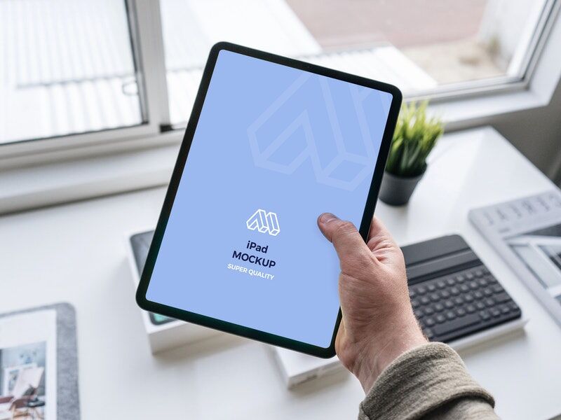 Mockup Showcasing Hand Holding iPad in a Office Table Scene